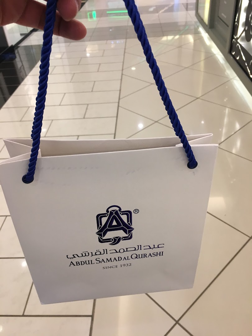 A white shopping bag with blue rope handles and the Abdul Samad Al Qurashi logo.