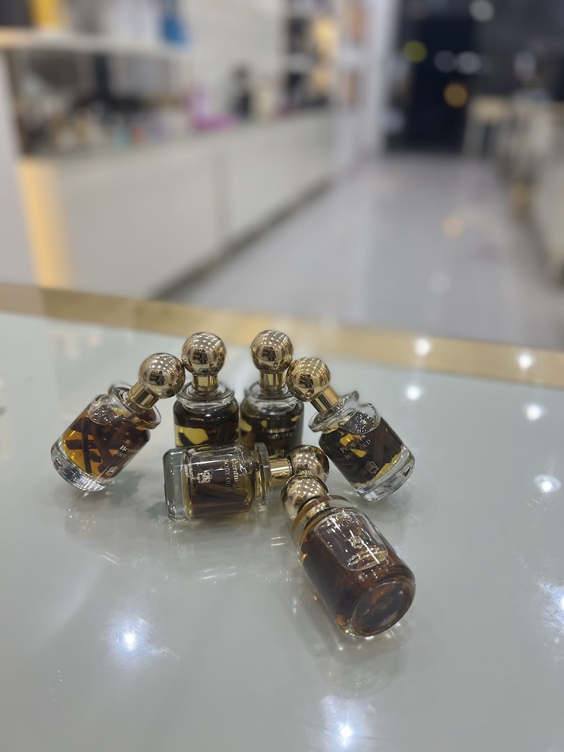Several small glass perfume bottles with gold caps are arranged on a reflective surface.