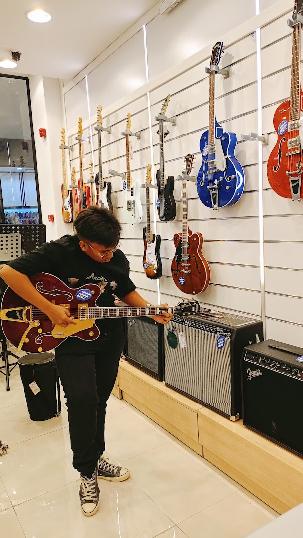 A person plays a guitar in a music store with many guitars on display.