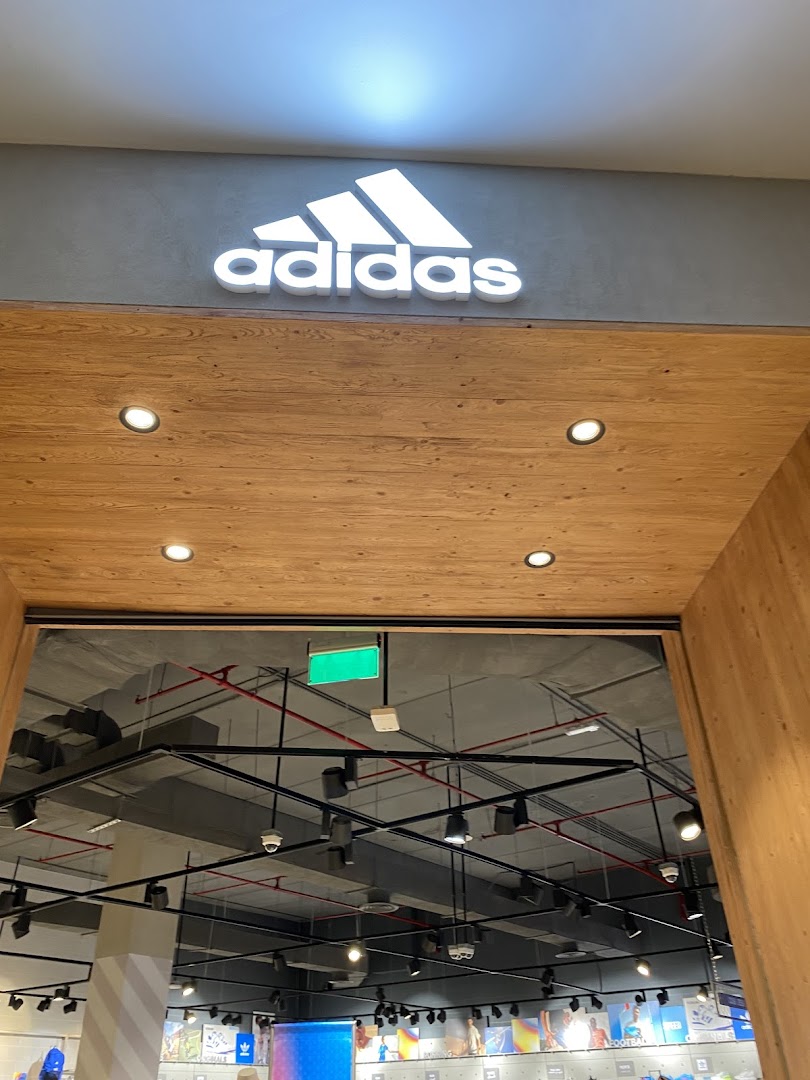 The entrance to an Adidas store with its iconic logo illuminated above a wooden facade.