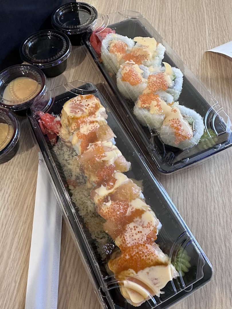 Two containers of sushi rolls with sauce and ginger on a wooden table.