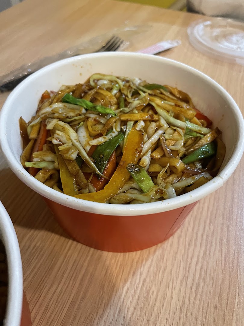 A close-up shot of a delicious noodle dish with vegetables in a red takeout container.