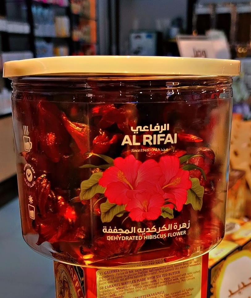 A clear plastic jar filled with dehydrated hibiscus flowers, branded "Al Rifai".
