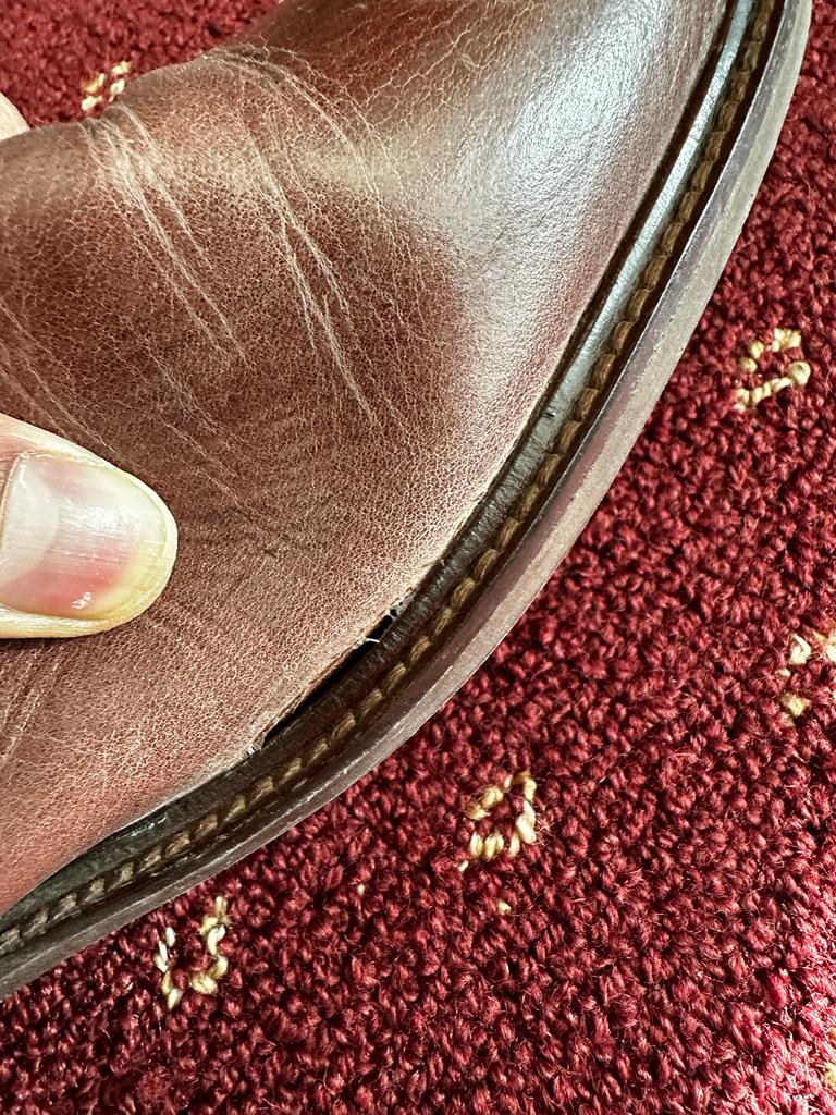 Close-up of a brown leather shoe's sole and stitching on a textured red surface.