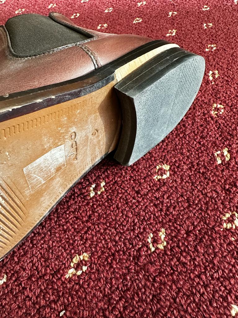 Close-up of the sole and heel of a brown leather shoe on a red carpet.