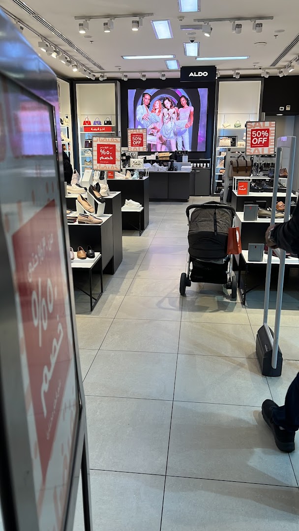 Interior view of an Aldo shoe store with displays of shoes and bags, and a large screen showing models.