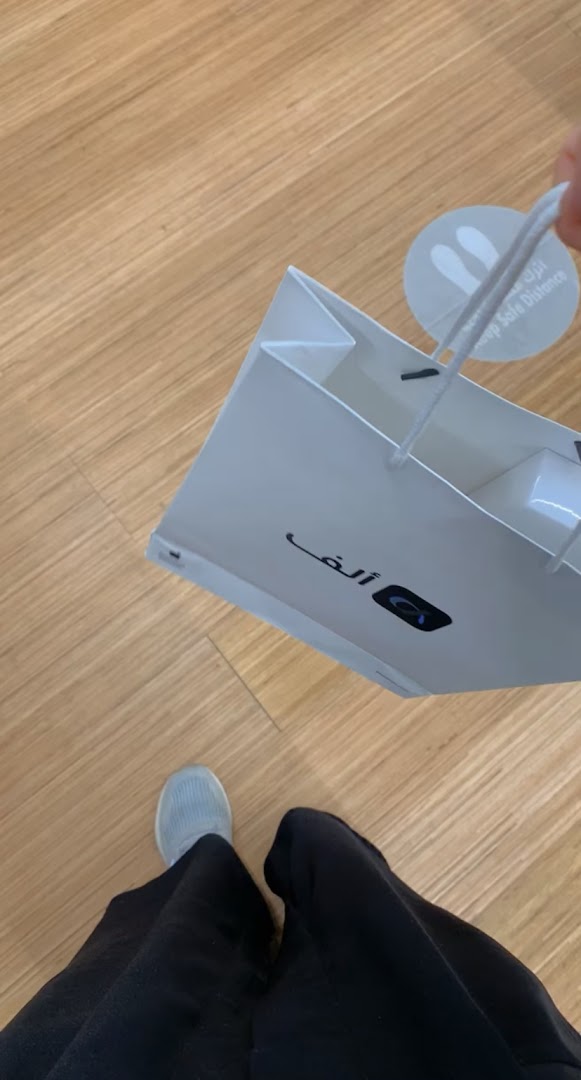 A person holding a white shopping bag with the Aleph logo and Arabic text.