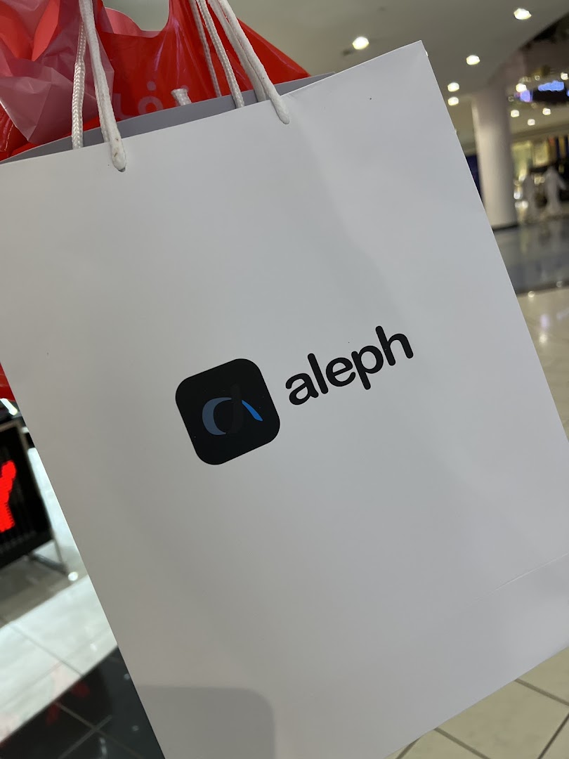 A white shopping bag with the Aleph logo and text, held with other shopping bags.