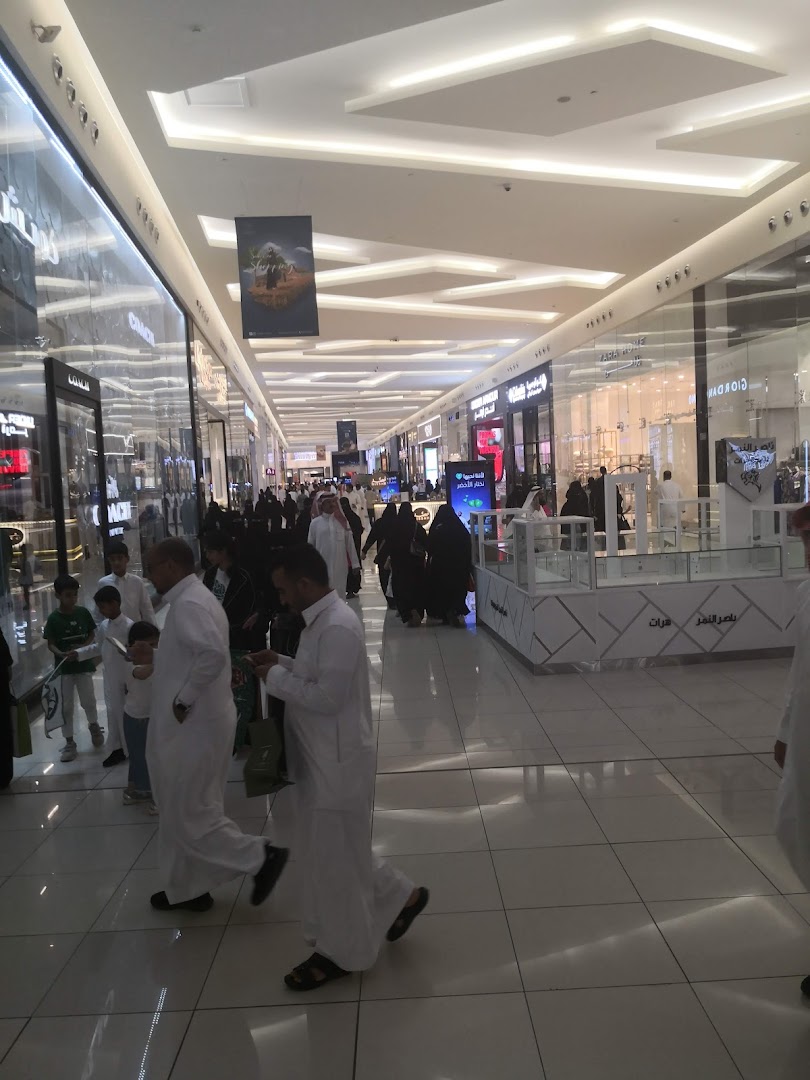 People walking through a brightly lit, modern shopping mall with various stores visible.