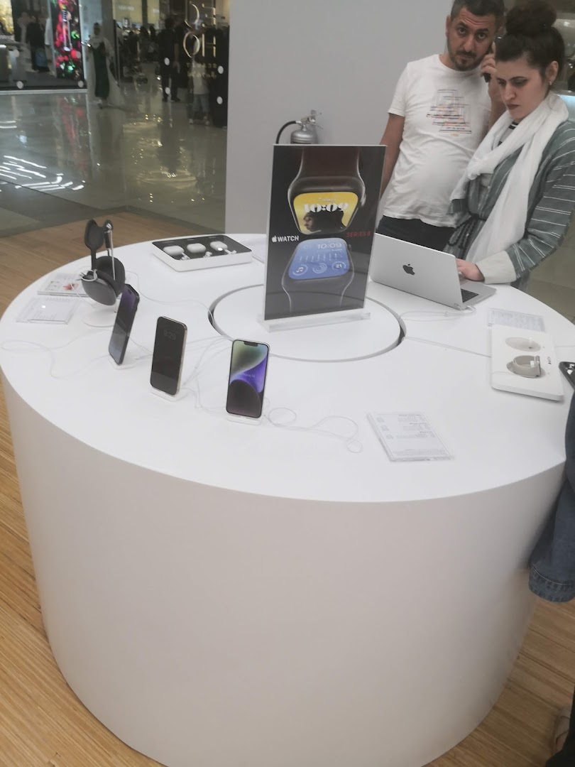 Customers examining Apple products on a display table in a modern retail store.
