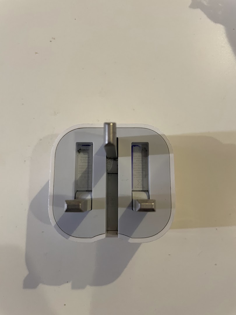 A close-up shot of a white Apple power adapter with UK-style pins.