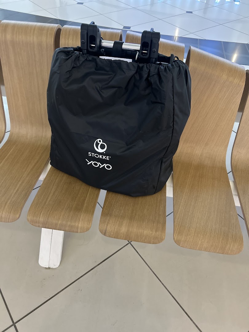 A black Stokke YOYO travel bag is placed on a wooden bench.