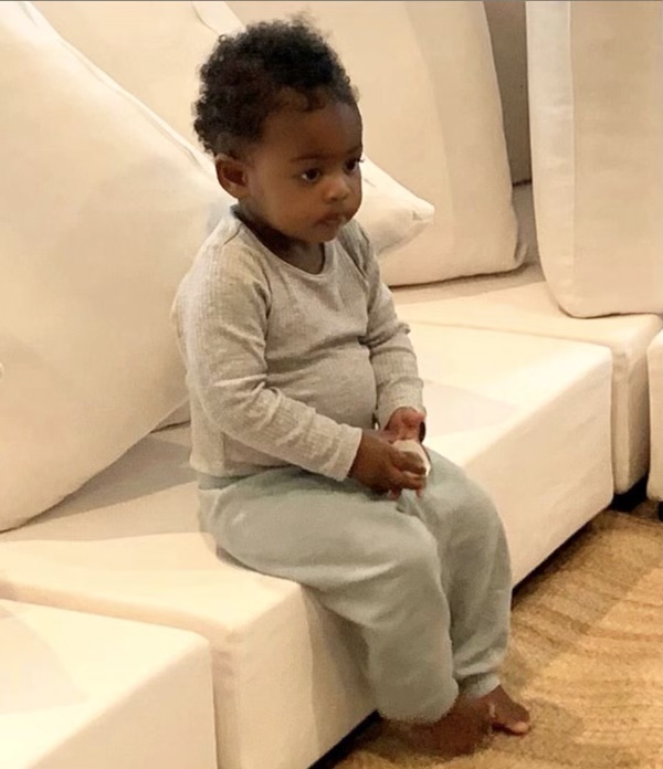 A young child sits on a white sofa, looking off to the side.