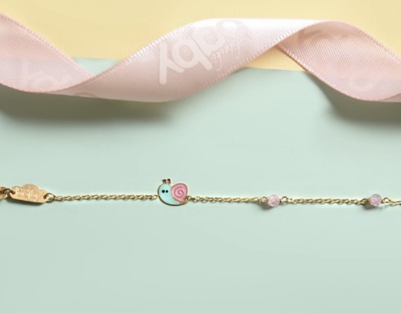 A delicate gold bracelet with a snail charm and pink beads, adorned with a pink ribbon.