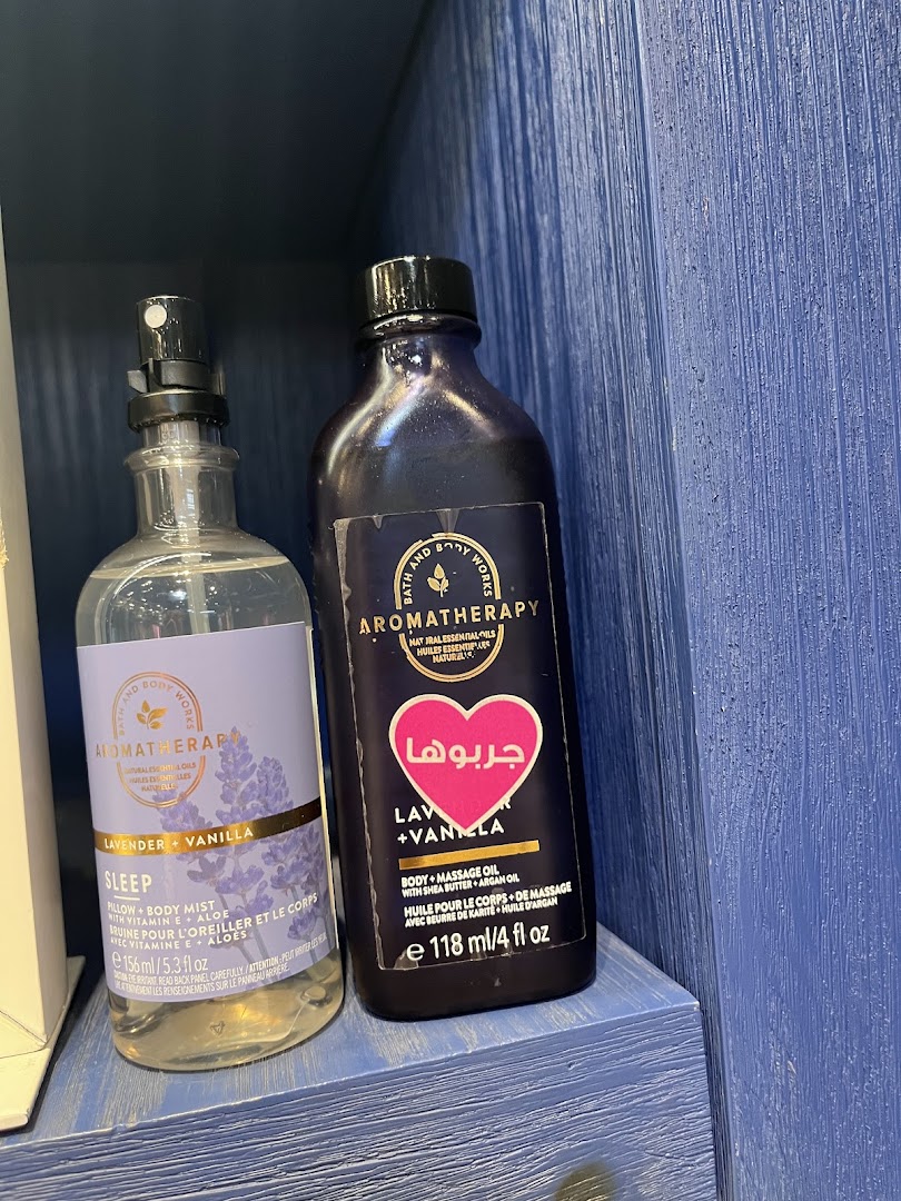 Two Bath & Body Works aromatherapy products, a pillow mist and massage oil, are displayed on a blue shelf.