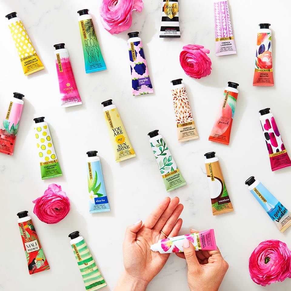 A collection of Bath & Body Works hand creams with floral and fruit designs, along with pink flowers.