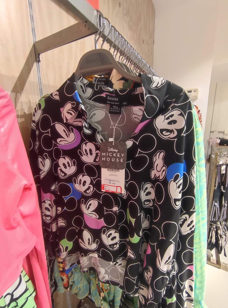 A black shirt with a colorful Mickey Mouse print hanging on a rack at Bershka.