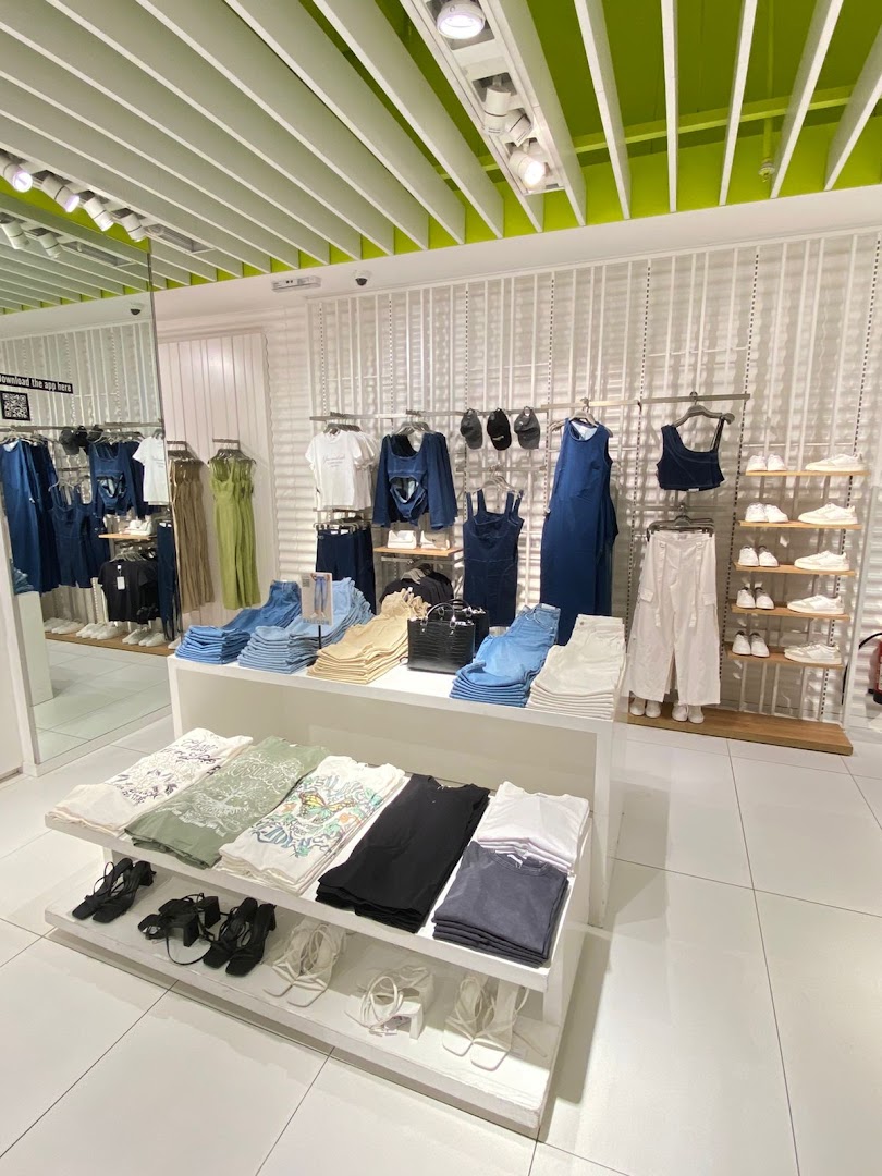 Interior view of a clothing store displaying folded t-shirts, jeans, dresses, and shoes.