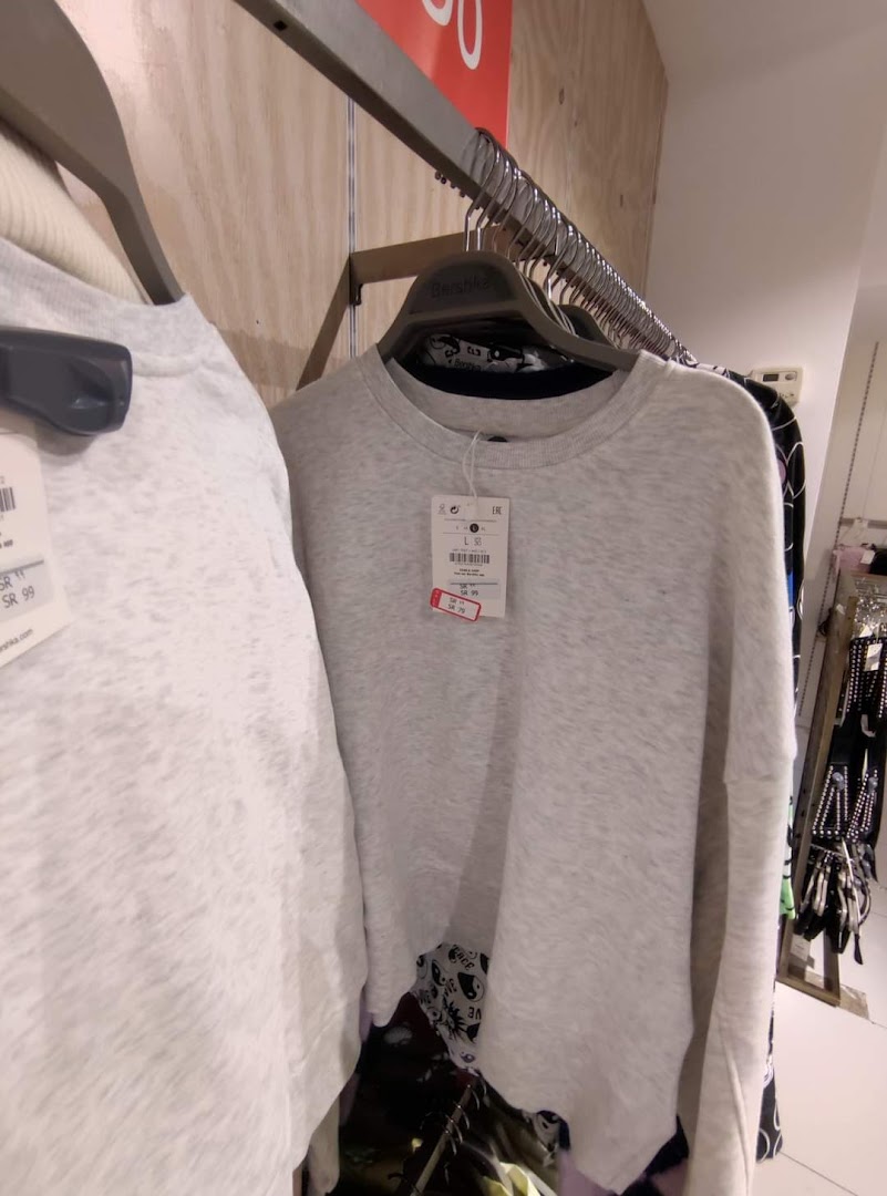 Close-up of light grey sweaters on hangers with price tags visible.