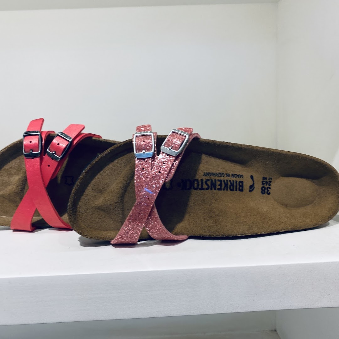 Two pairs of Birkenstock sandals, one pink and one glittery pink, displayed on a white shelf.