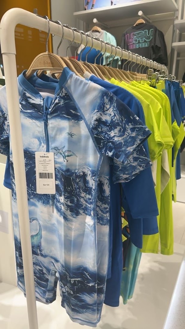 A rack of children's swimwear featuring dinosaur and wave prints, with bright colors.