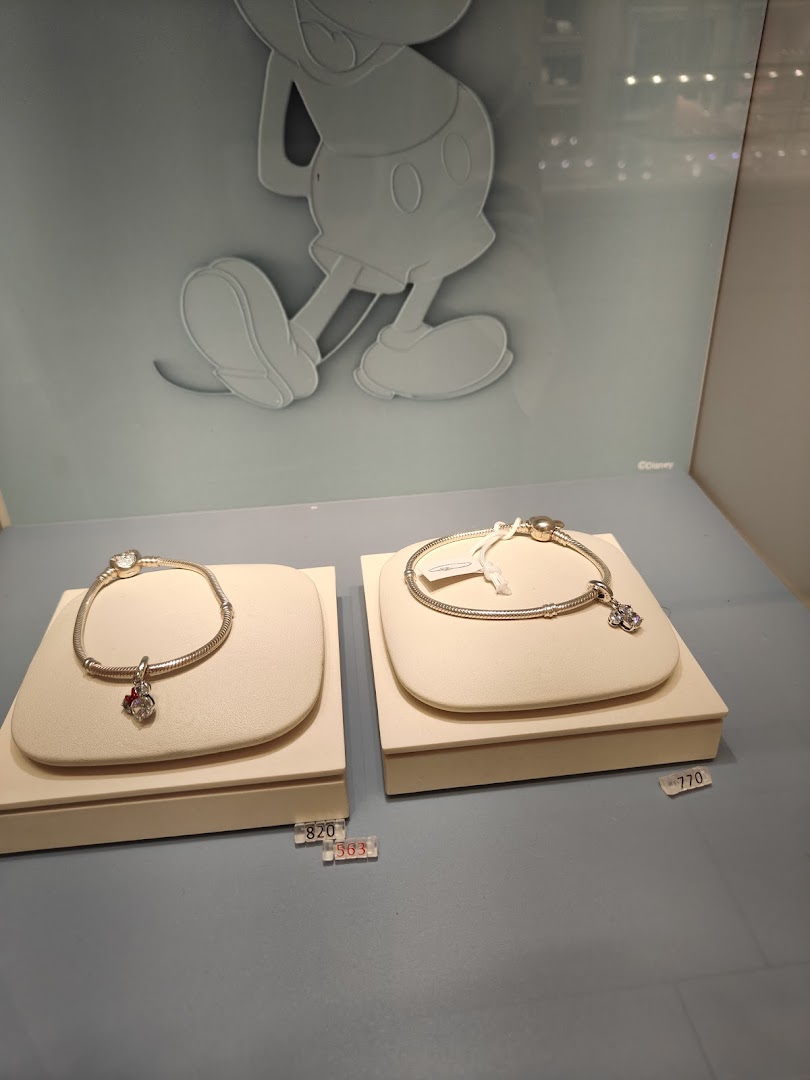 Two Pandora charm bracelets are displayed on stands, with a Mickey Mouse silhouette in the background.