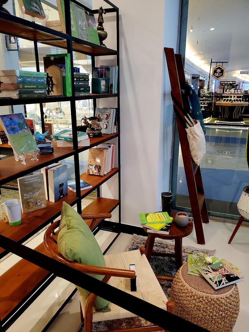 A cozy reading nook with bookshelves, a chair, and a small table displaying books and a mug.