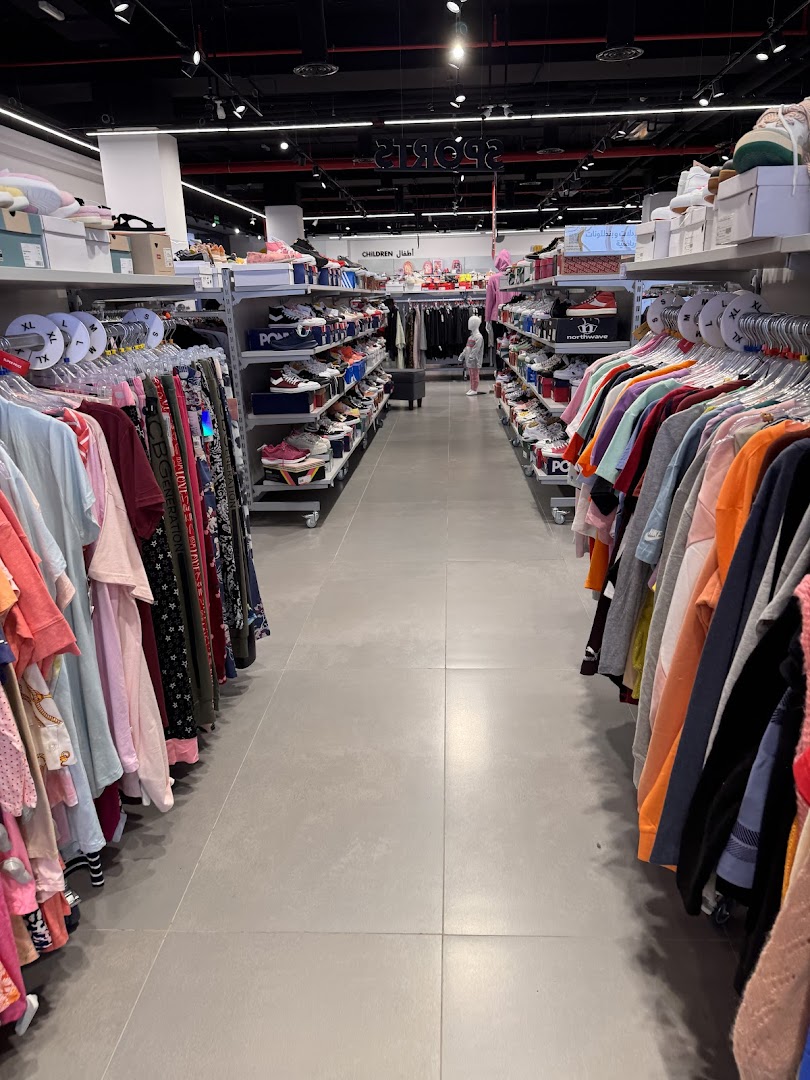 A wide aisle in a clothing store, showcasing racks of apparel and shelves of shoes.