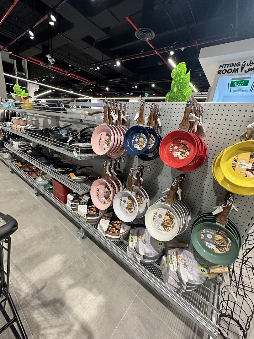 A display of colorful frying pans and kitchenware on shelves in a retail store.