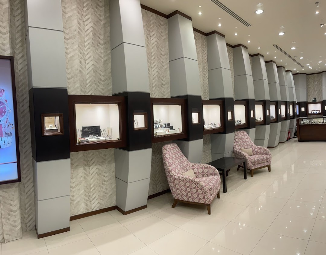 Interior view of Ibrahim AlQurashi Perfumes shop showcasing display cases with watches and seating.