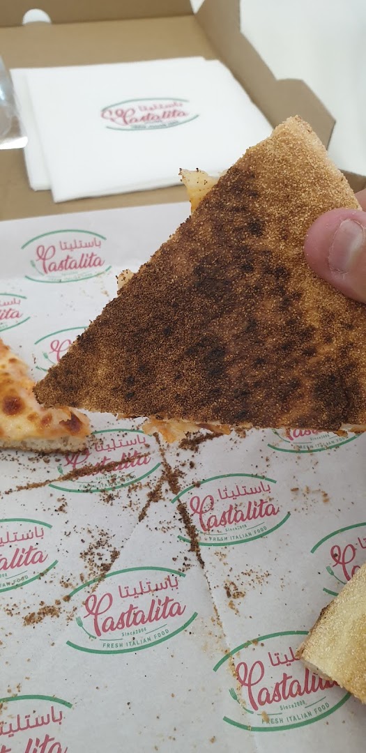 A slice of pizza with a crispy crust is held over a pizza box with the shop's logo.