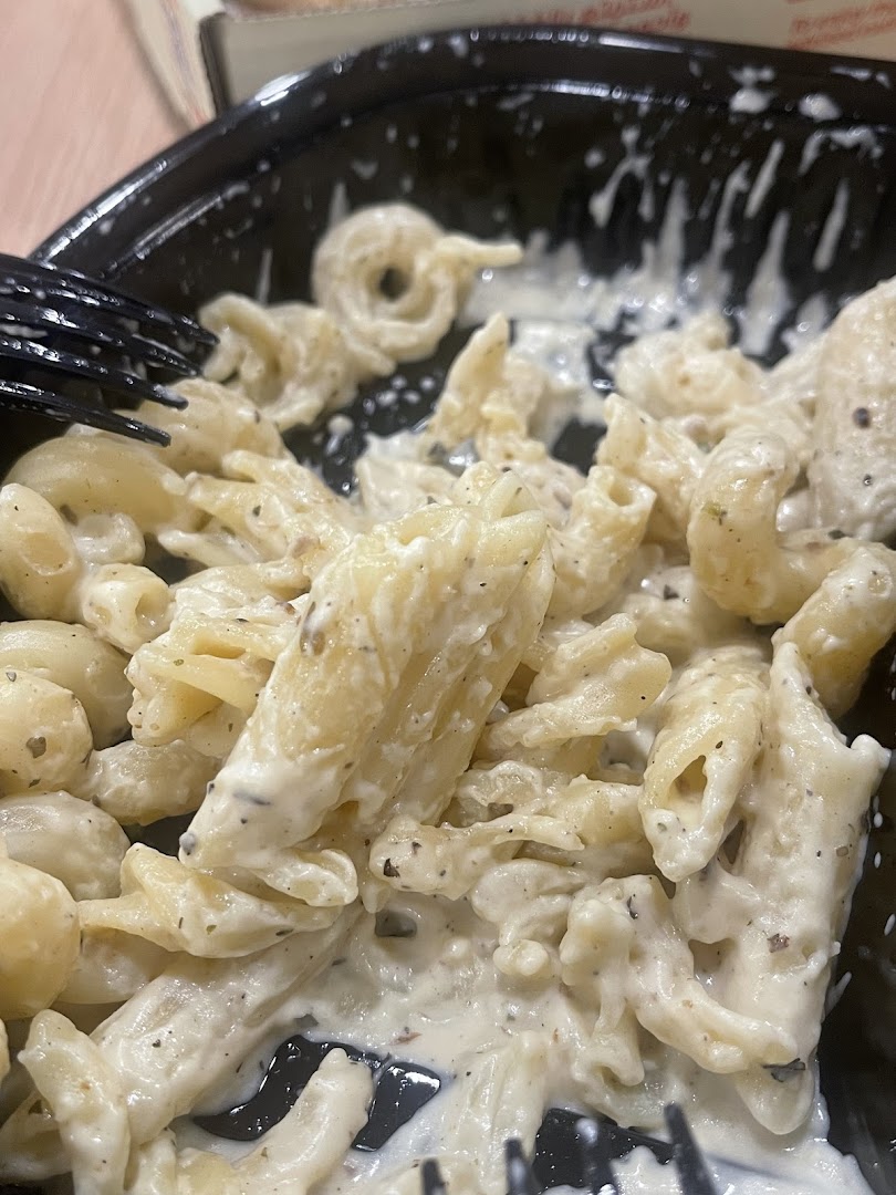 A close-up shot of creamy pasta with penne and other pasta shapes, served in a black container.
