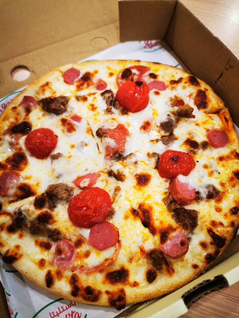 A delicious pizza with tomatoes, sausage, and meat toppings in a cardboard box.