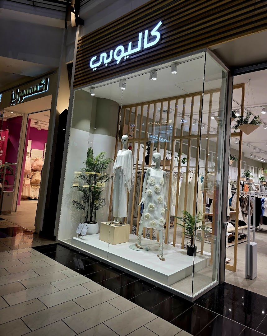 Calliope fashion store window display featuring mannequins in elegant white outfits and greenery.