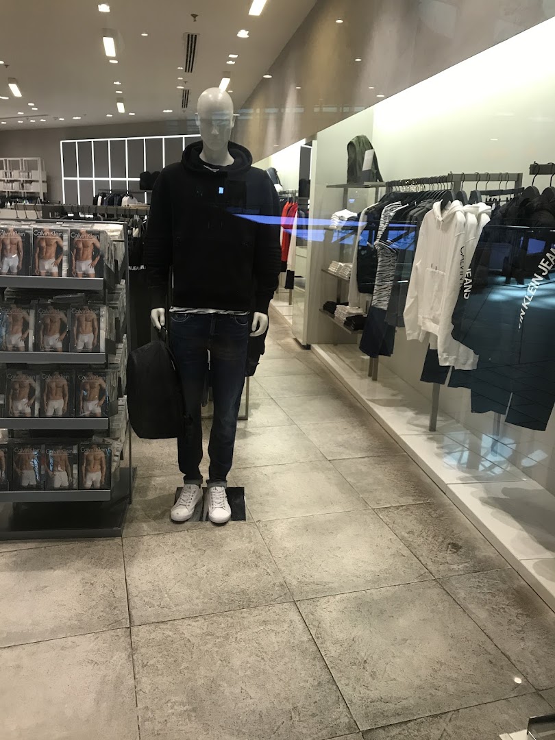 A mannequin dressed in Calvin Klein clothing stands in a well-lit store with merchandise displayed.