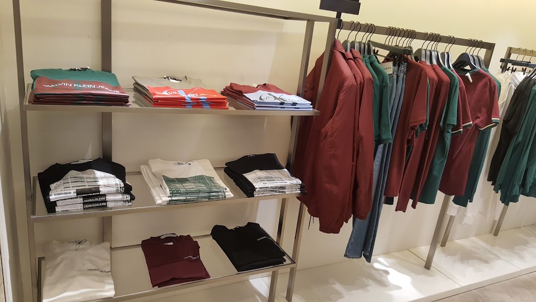 Calvin Klein store interior displaying folded t-shirts and hanging jackets and shirts.