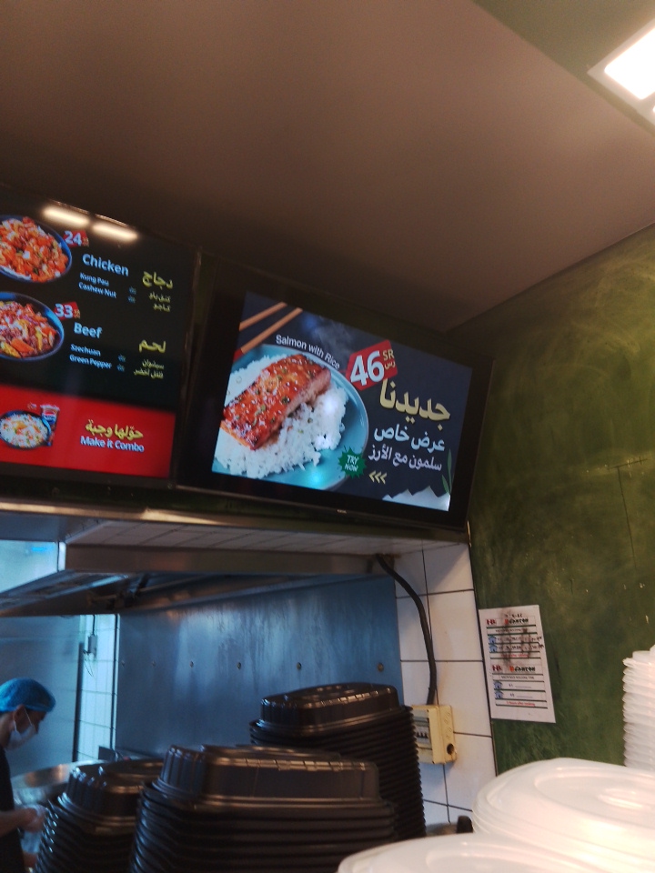 A digital menu board displays food items like chicken and beef, with a special offer for salmon with rice.