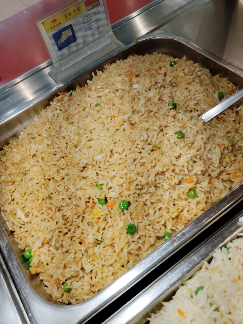 A close-up of a steaming tray of fried rice with peas and carrots.