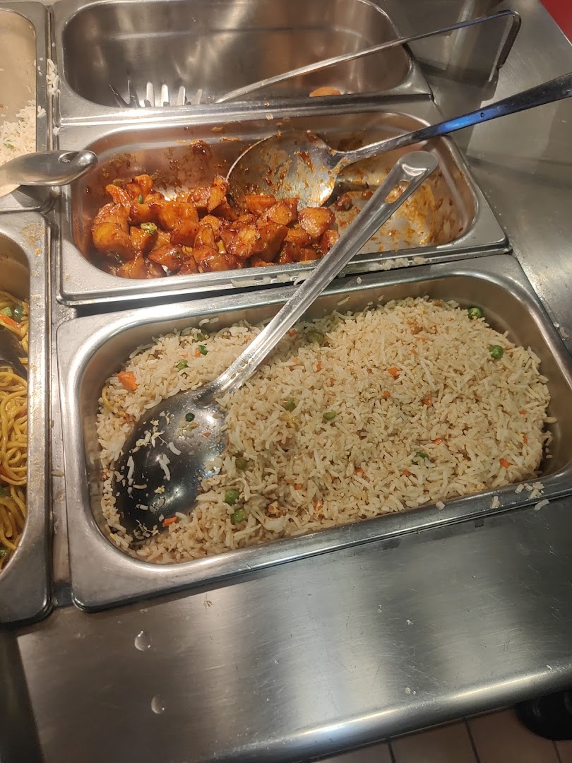 A close-up of a food service counter with trays of fried rice and glazed chicken.