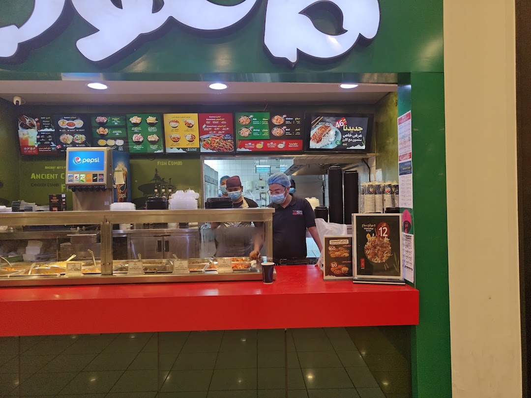 A food counter with various dishes displayed and staff serving customers.
