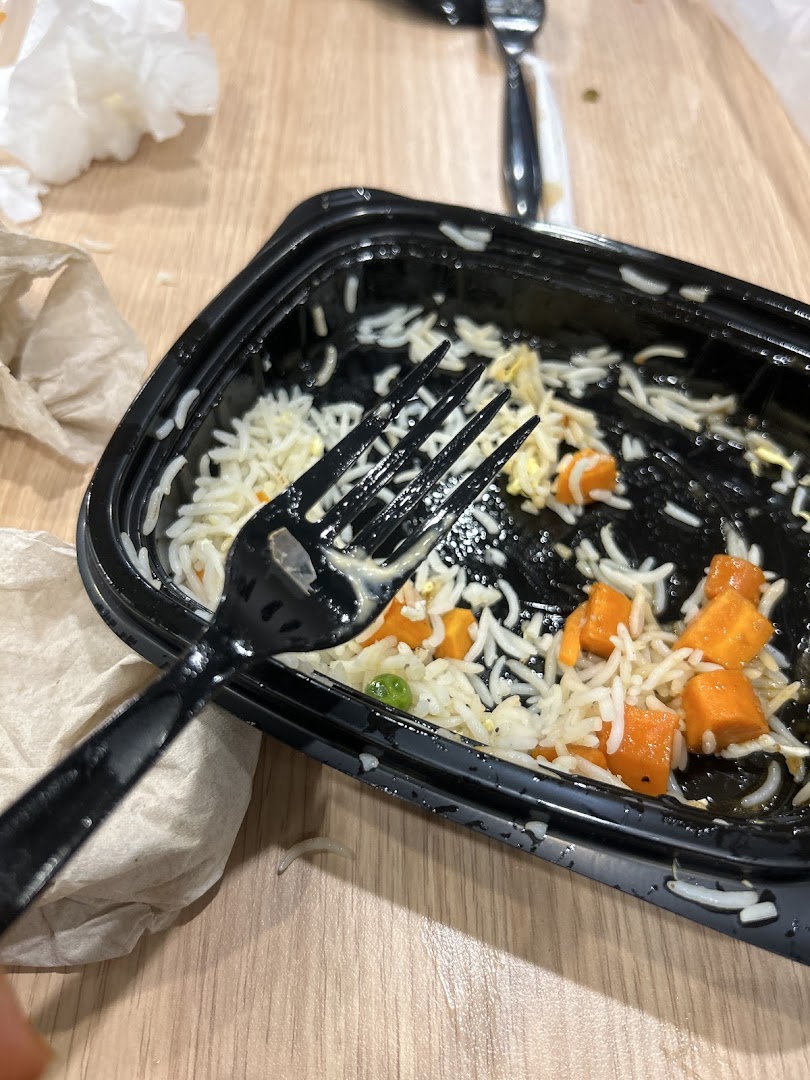 A close-up of a nearly empty takeout container with rice, carrots, and peas, and a fork resting on top.