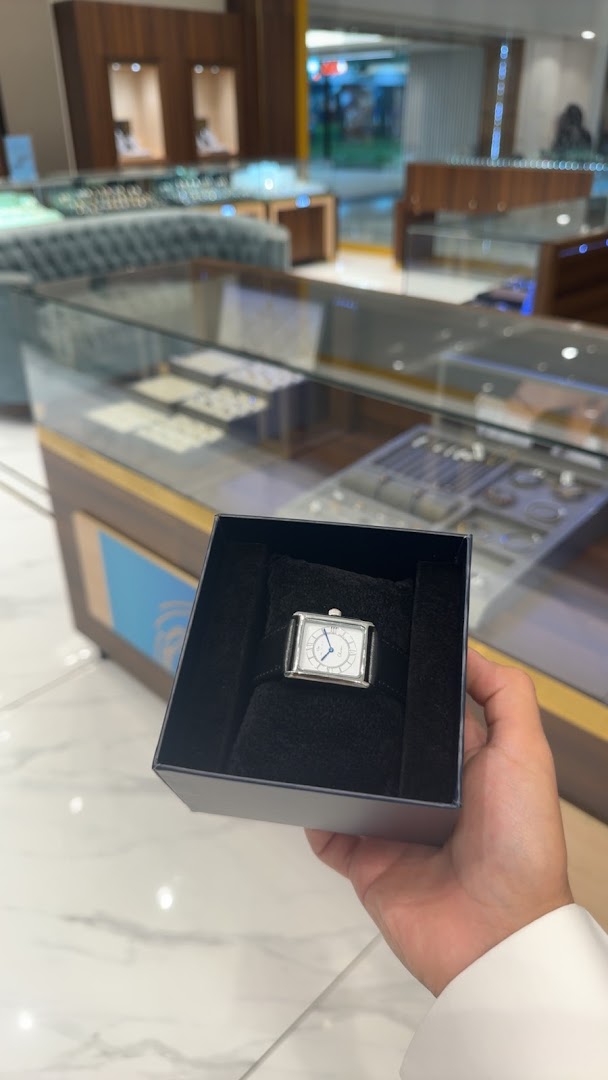 A hand holds a watch in a box inside a jewelry store.