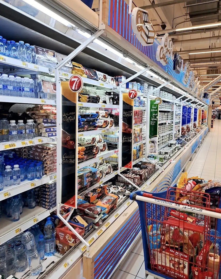 Aisle of a supermarket with shelves stocked with bottled water and packaged snacks.