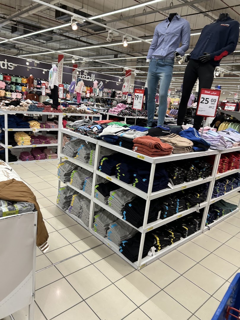 Interior view of a hypermarket displaying folded clothing on shelves and mannequins.