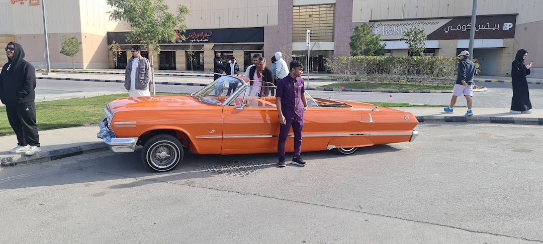 An orange classic convertible car parked outside a shopping mall with people around.