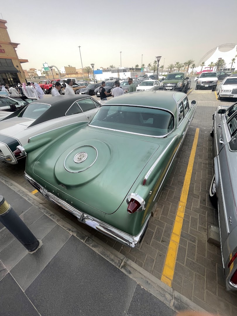 A collection of classic cars parked in a lot, with people gathered around.