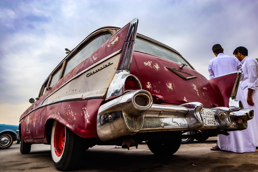 A vintage red Chevrolet station wagon with chrome accents and two men in traditional attire.