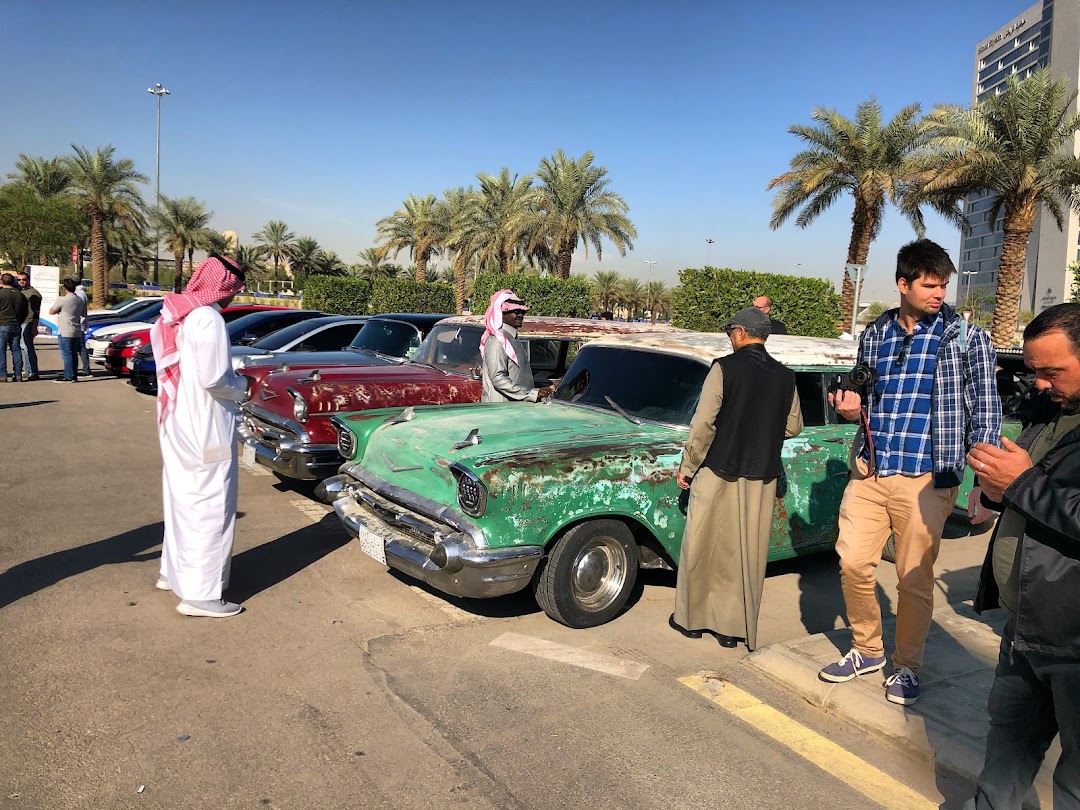 People gather around vintage cars parked outdoors on a sunny day.