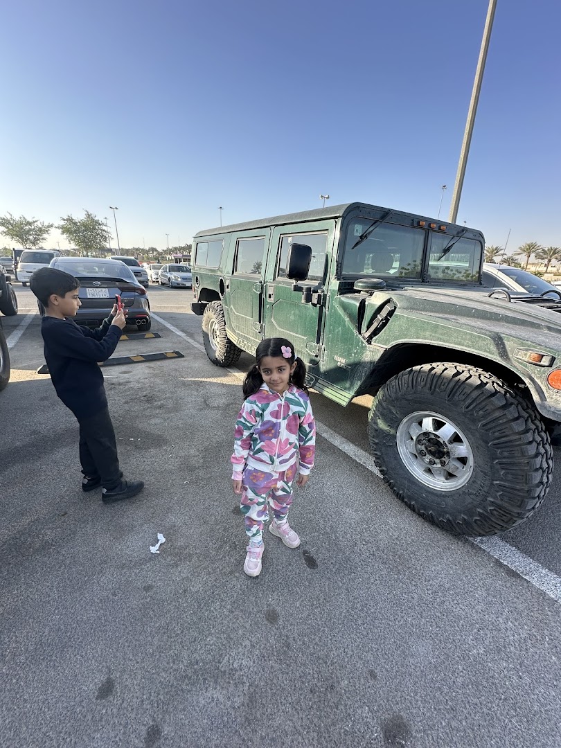 A boy takes a photo of a green Hummer while a girl stands next to it.