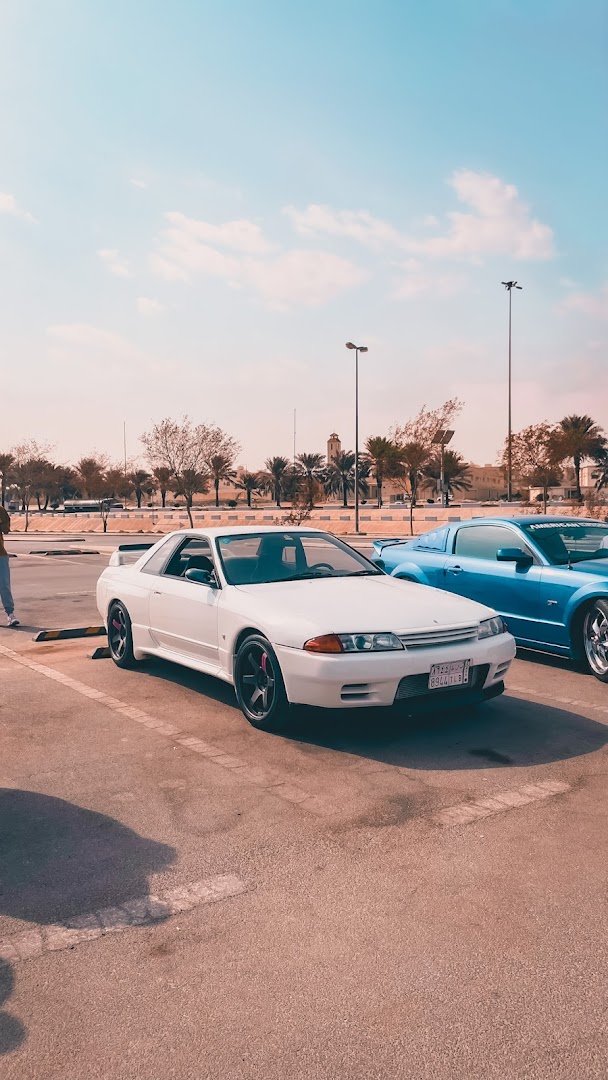 Two stylish cars, a white Nissan Skyline and a blue Ford Mustang, parked outdoors.